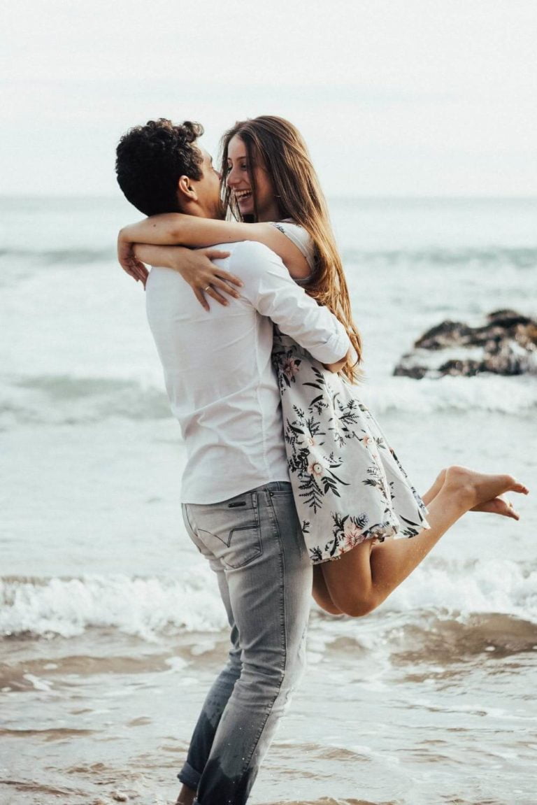 a man and woman holding each other on a beach