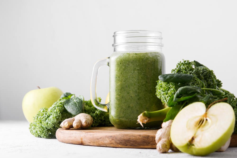 a glass of green liquid next to a whole vegetable and a whole vegetable